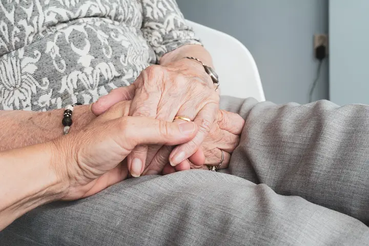 A pair of hands gently holding the hands of an older adult