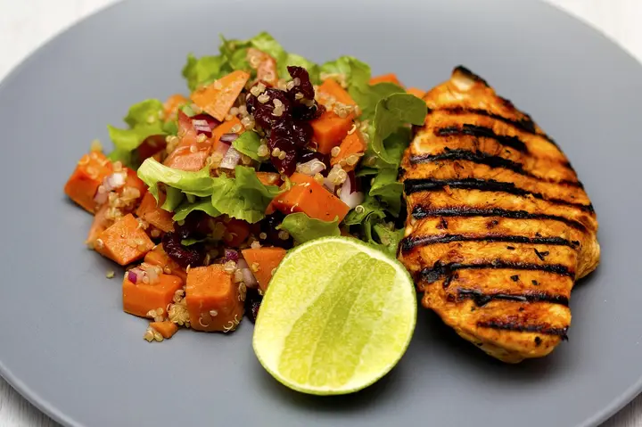 A plate of grilled chicken with a quinoa and fresh vegetable salad