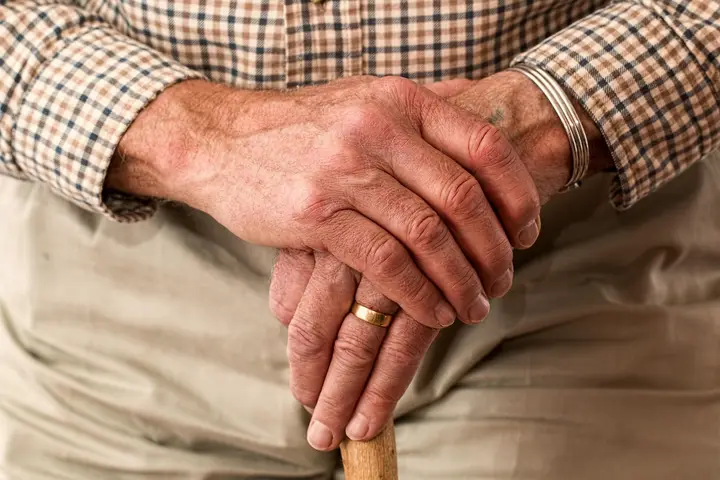 An older adult's hands resting on a wooden walking cane